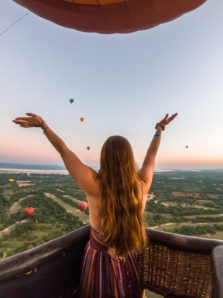 Woman with hands in air in a hot air balloon at sunrise 